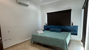 Un dormitorio con cama, ventana con cortina oscura, luz de techo y unidad de aire acondicionado.