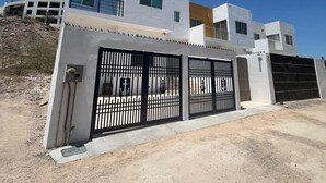 Una casa moderna de dos pisos con entrada protegida por un portón y un cielo azul despejado.
