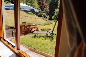 Blick durch eine Glastür auf einen Essbereich mit Außenplätzen, darunter ein Tisch und Stühle, sowie zwei Peterstaler Sonnenschirme im Hintergrund.