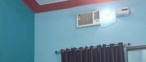 A bedroom with a bed, a bedside table, a ceiling fan, an air conditioning unit, and a window with curtains.