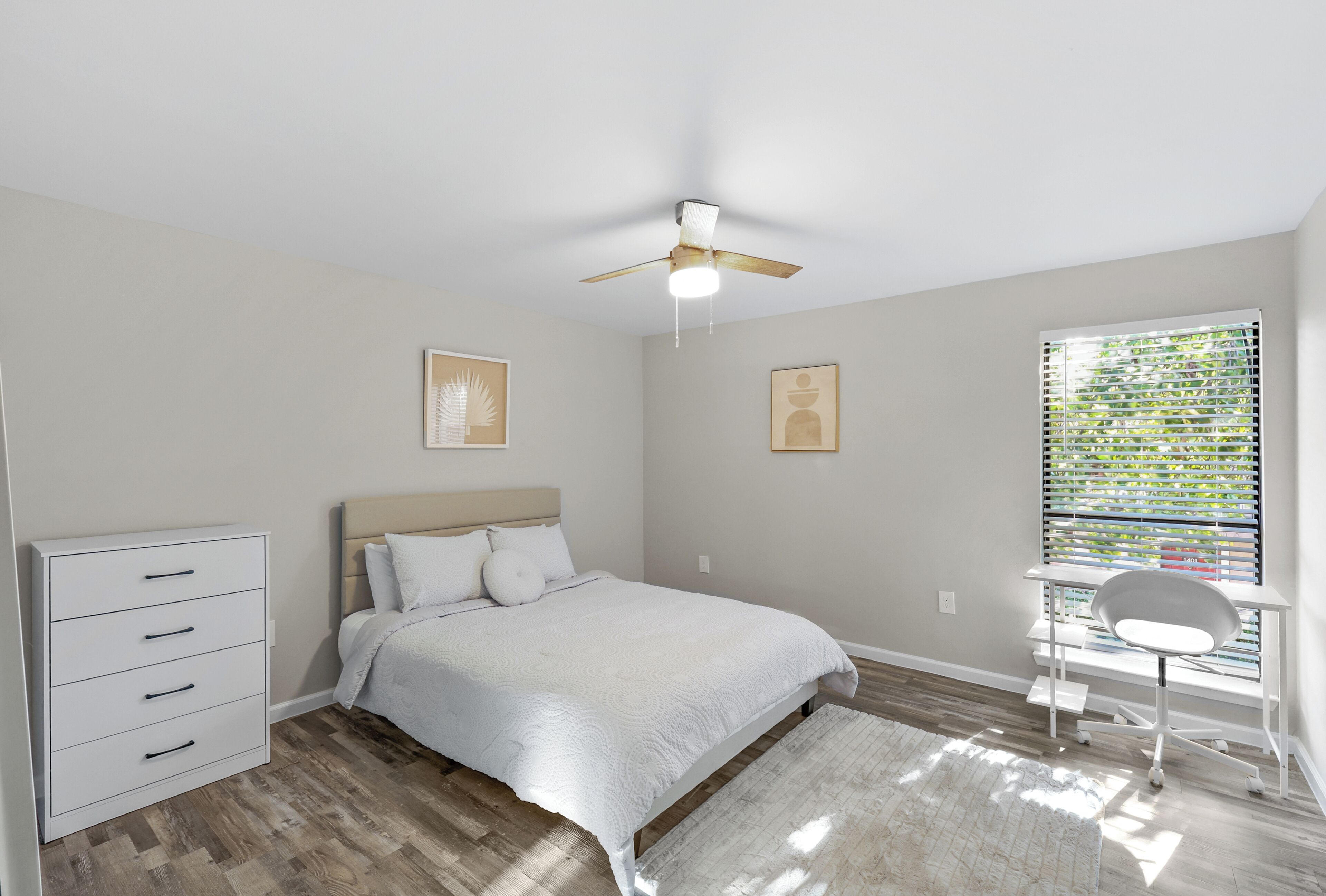 A bedroom with a bed, a desk, a chair, a ceiling fan, and a window with blinds.