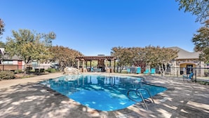 Une piscine rectangulaire agrémentée d’une pergola et de chaises longues, entourée d’arbres et d’une clôture.