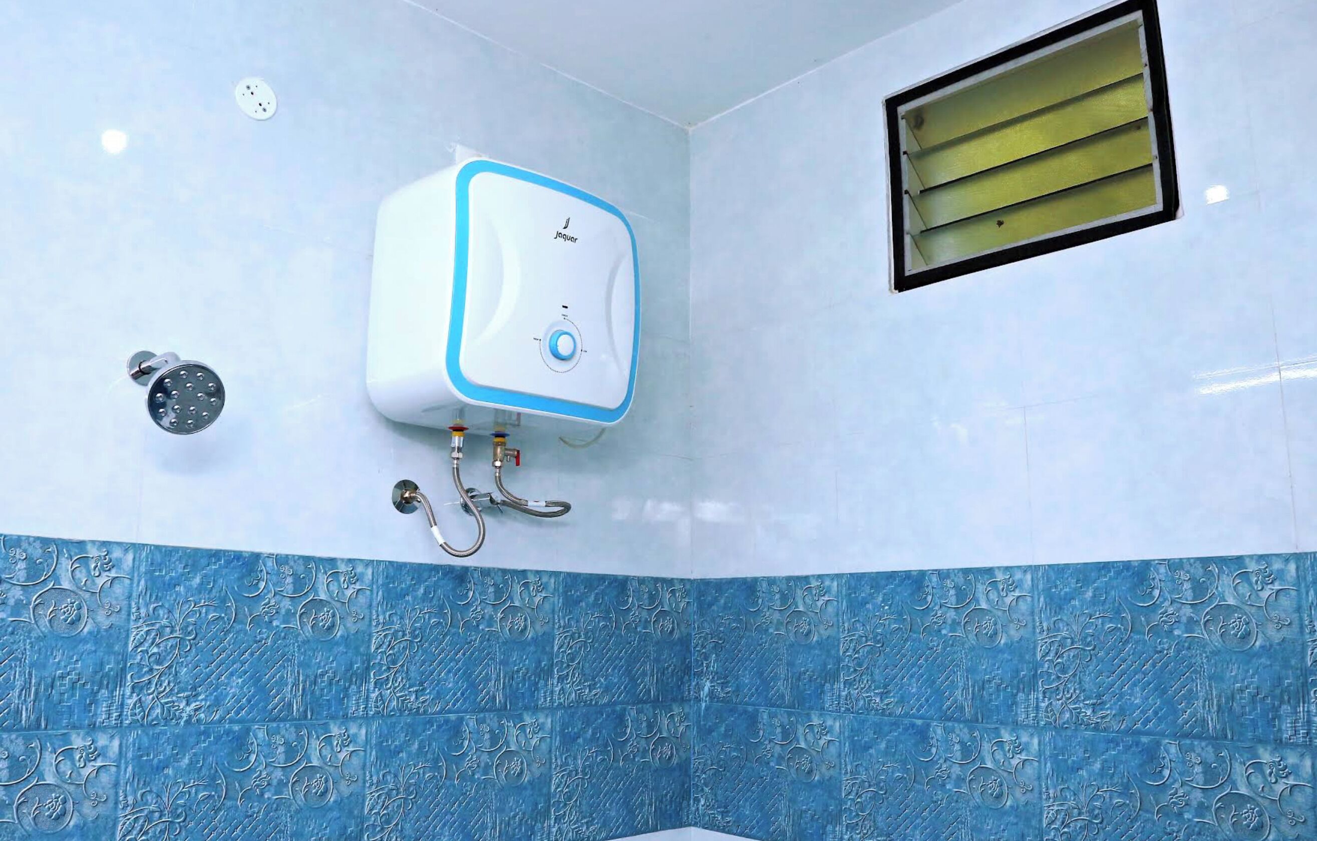 Un baño con calentador de agua instalado en la pared, una ducha y una rejilla de ventilación.