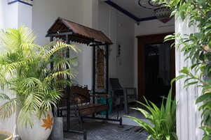 Un área de estar al aire libre con techo, un banco, una silla y una estructura metálica decorativa.