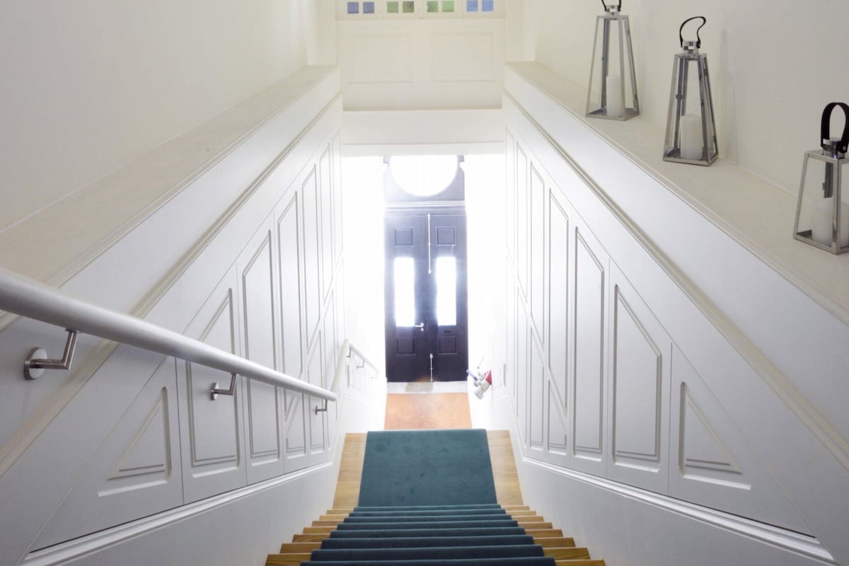 Una escalera con paredes blancas, un suelo de moqueta verde y vistas a una habitación en la parte superior.