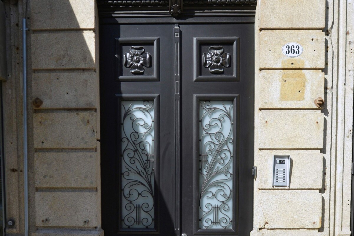 Una puerta doble negra con paneles de vidrio ornamentados, fachada de piedra y placa con un número.