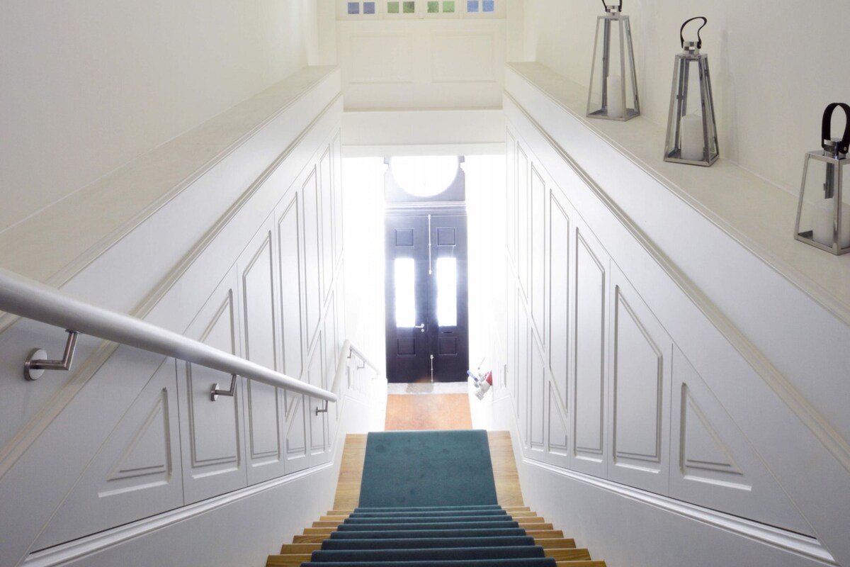 Una escalera con paredes blancas, un suelo de moqueta verde y vistas a una habitación con una puerta en la parte superior.