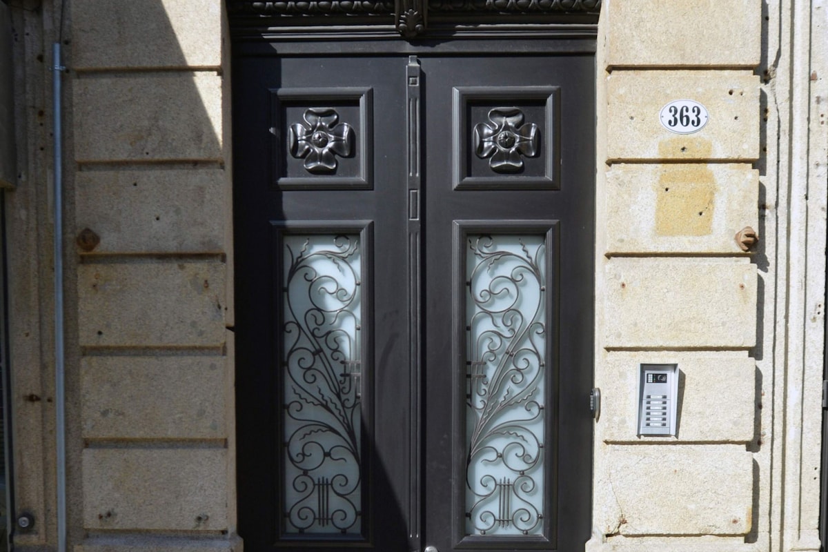 Una puerta doble negra con paneles de vidrio ornamentados, fachada de piedra y placa con un número.