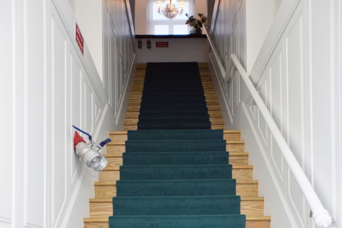 Una escalera con escalones de madera y alfombra color turquesa, que conduce a un rellano con candelabro.