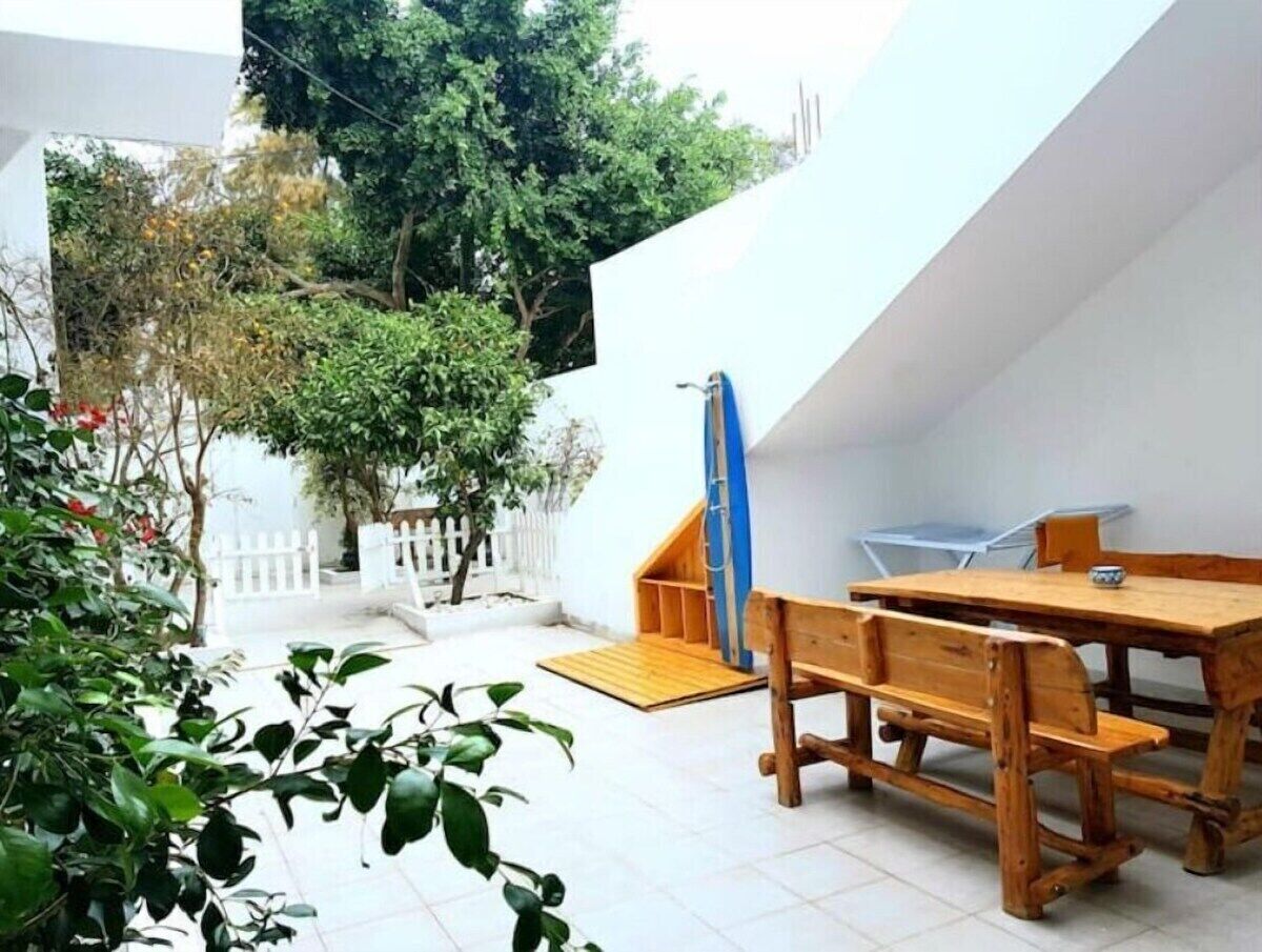 A wooden table and benches in a courtyard with a white wall and a blue door.