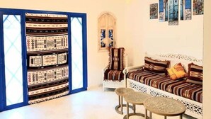 A cozy room with a patterned sofa, a small table, and a chair. There is a bookshelf with patterned books and a decorative wall hanging. - Welcome to Dar Jaafar! Cozy Arabesque Style Holiday House in la Marsa Tunisie (La Marsa)