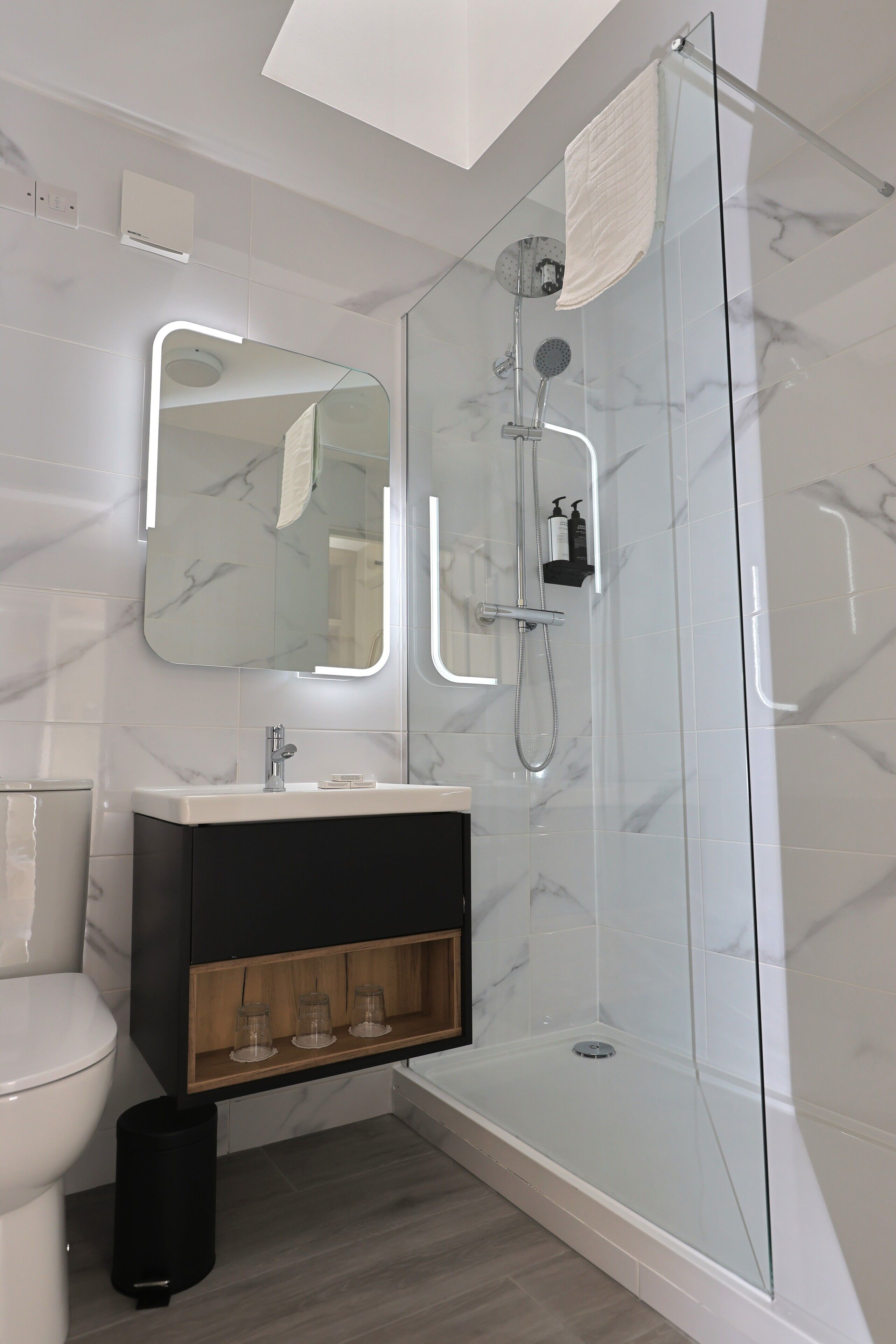 A modern bathroom with a glass-enclosed shower, a white toilet, a vanity with a mirror, and marble-patterned walls.