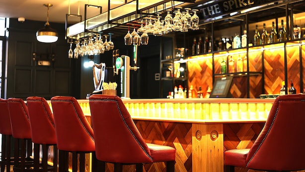 A bar with red chairs, a wooden bar counter, and a sign reading "THE SPIRE". - The Maiden City Hotel (Londonderry)