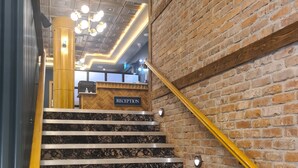 A staircase with a reception desk at the top, a brick wall, and a modern ceiling design. - The Maiden City Hotel (Londonderry)