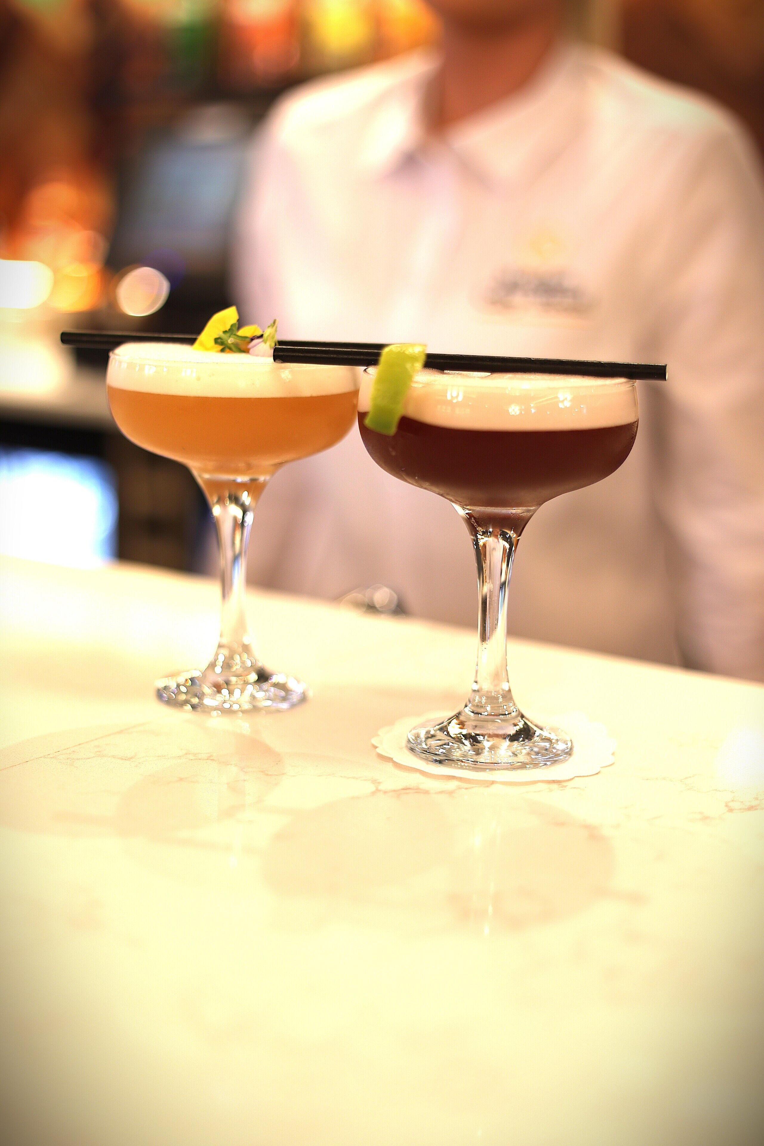 Two cocktails on a bar counter with a blurred background.