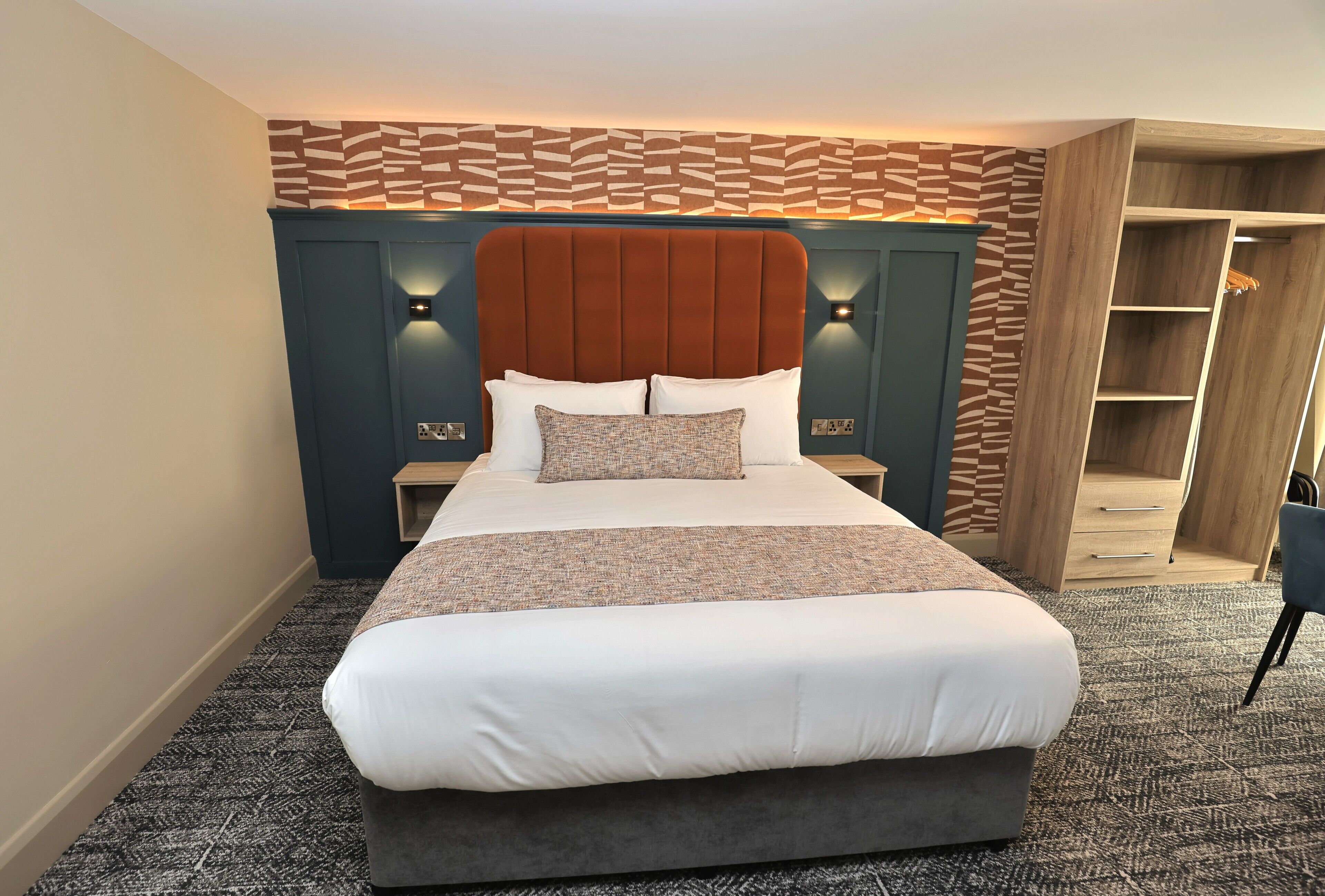 A neatly made bed with a headboard, two bedside tables, and a built-in wardrobe with drawers.