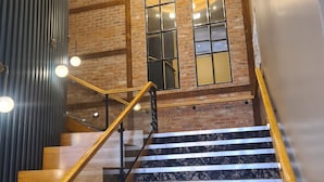A staircase with wooden handrails and marble steps, leading to a room with brick walls and large windows. - The Maiden City Hotel (Londonderry)