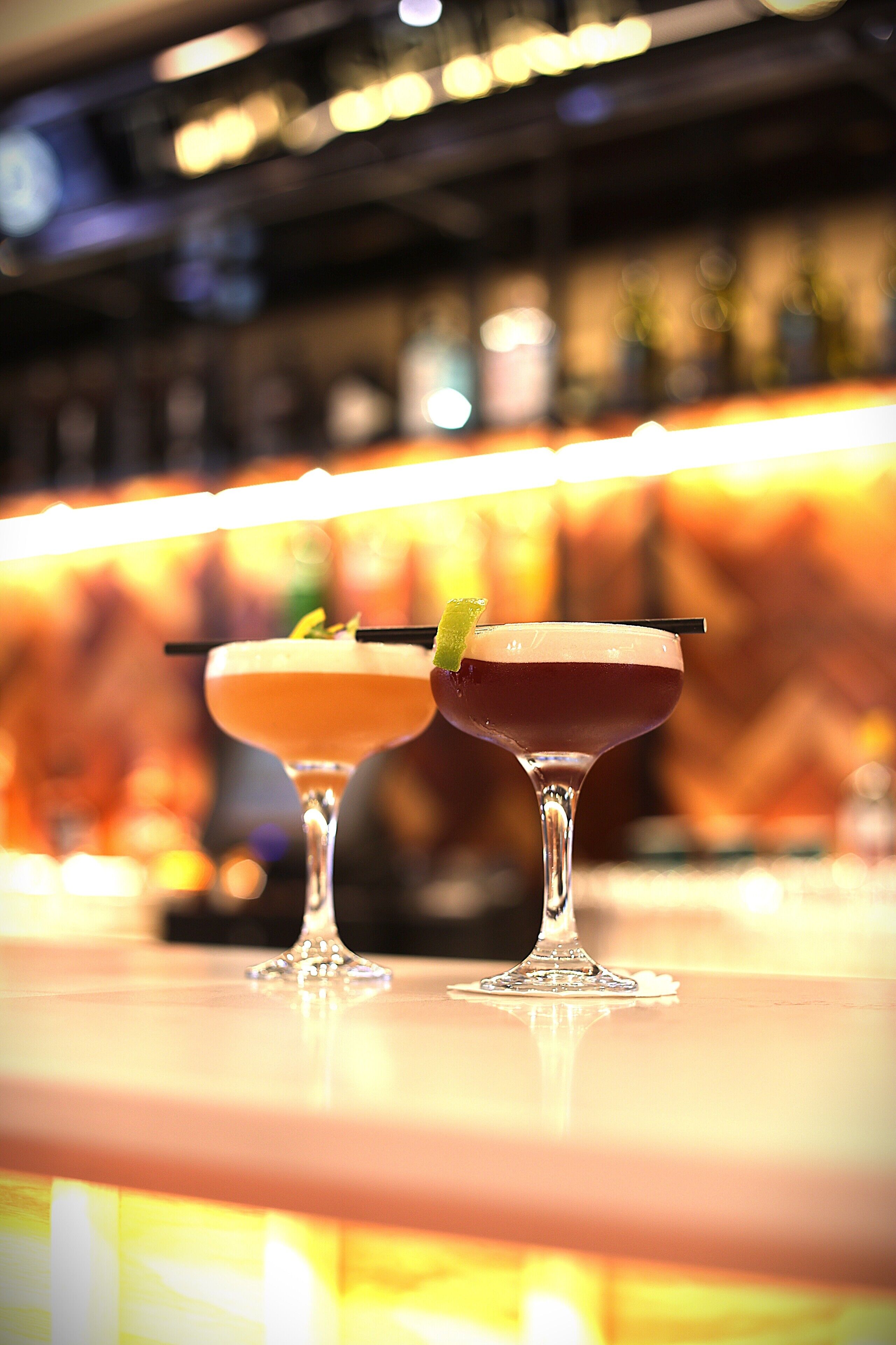 Two cocktails on a bar counter with a blurred background.
