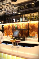 A bar area with a wooden herringbone wall, a cash register, and a variety of liquor bottles.