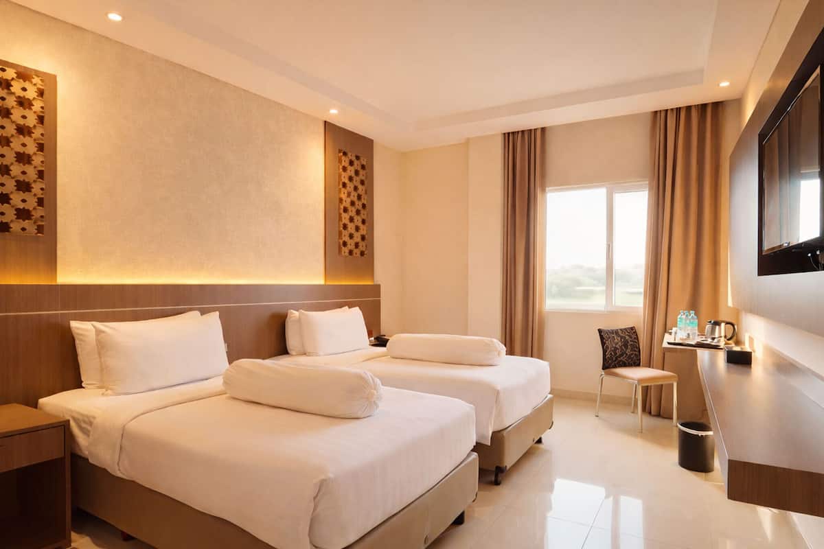 A hotel room with two beds, a desk, a chair, a TV, and a window with curtains.
