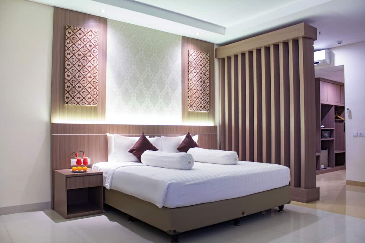 A modern hotel room with a large bed, a nightstand with a fruit bowl, and a wardrobe.