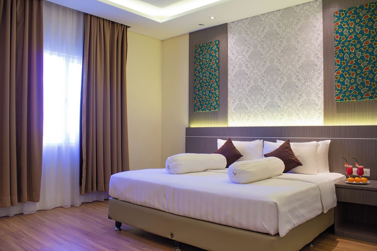 A hotel room with a large bed, a nightstand with a drink, and a wall with decorative patterns.