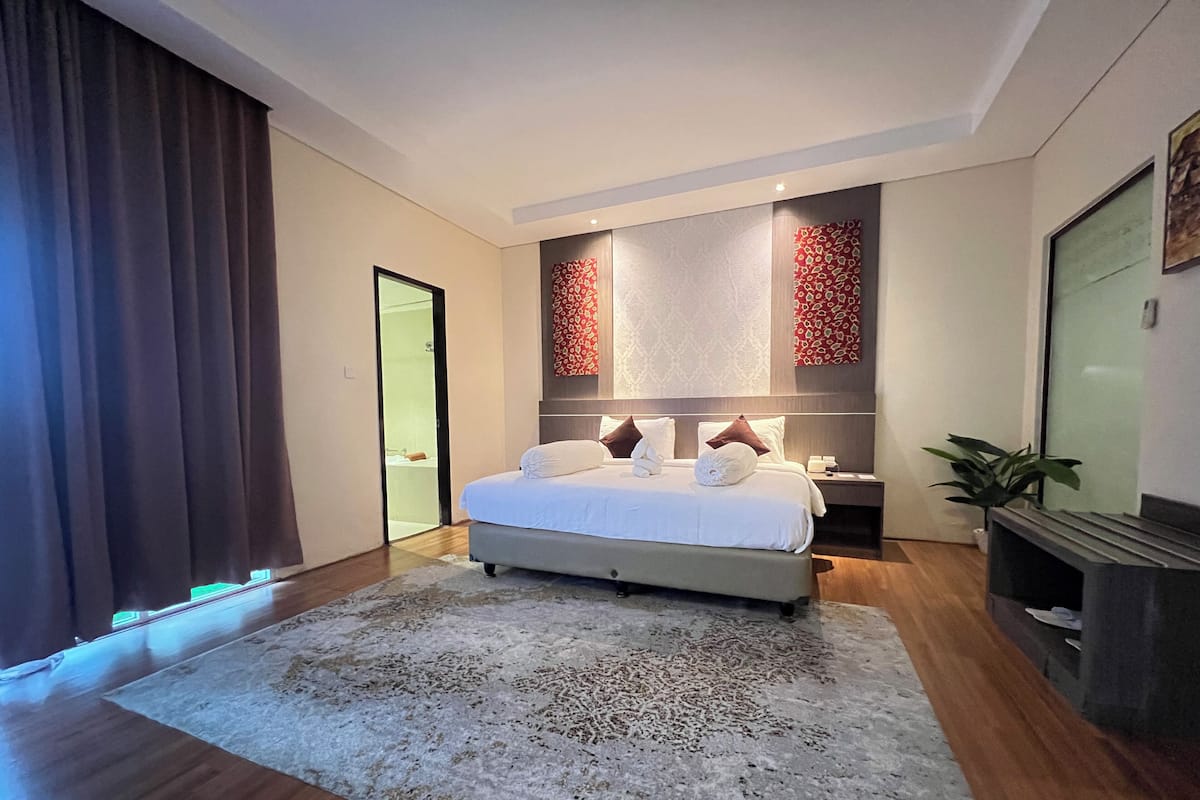 A modern bedroom with a large bed, a nightstand, a mirror, and a plant.