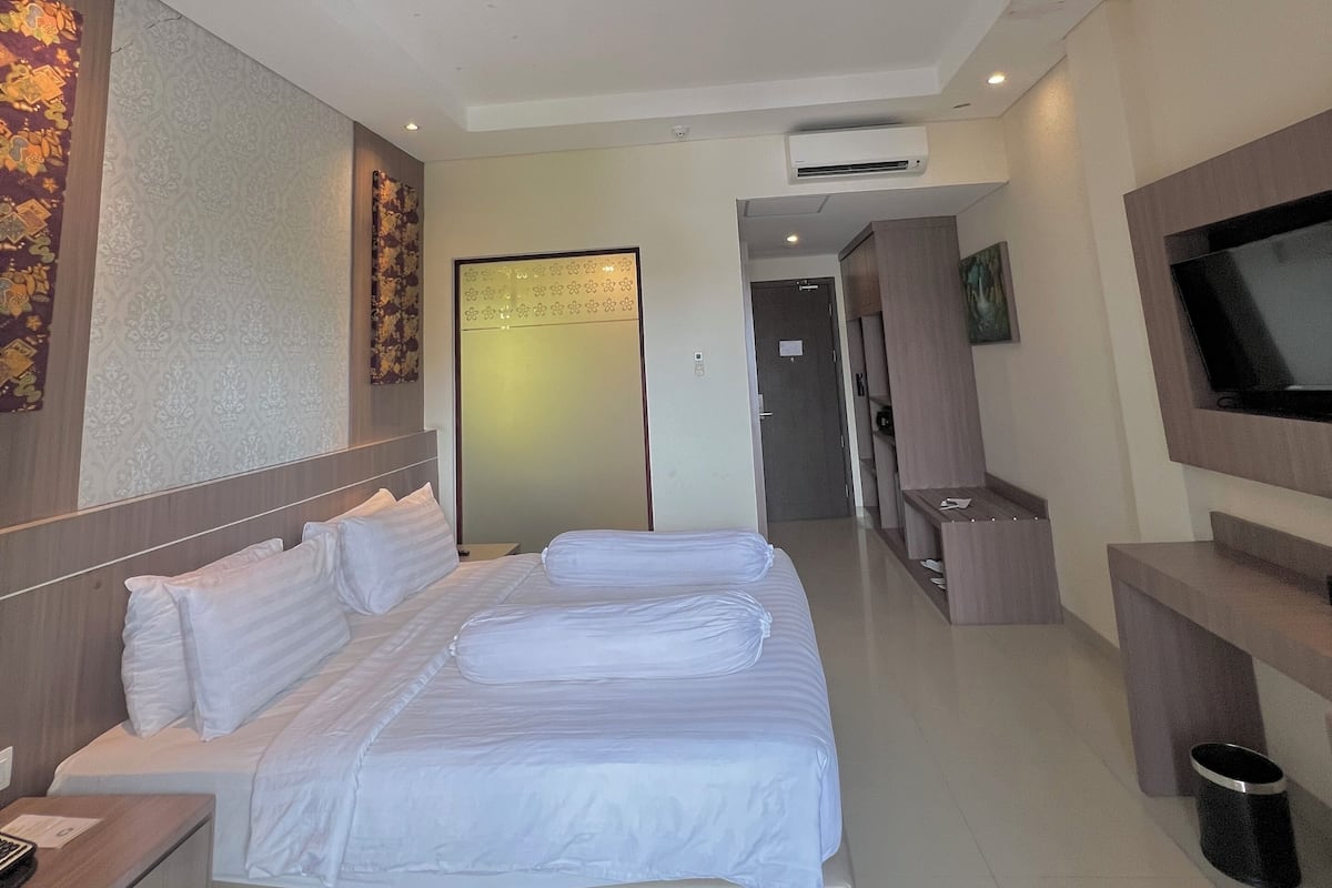 A hotel room with a large bed, a TV mounted on the wall, and a desk with a chair.