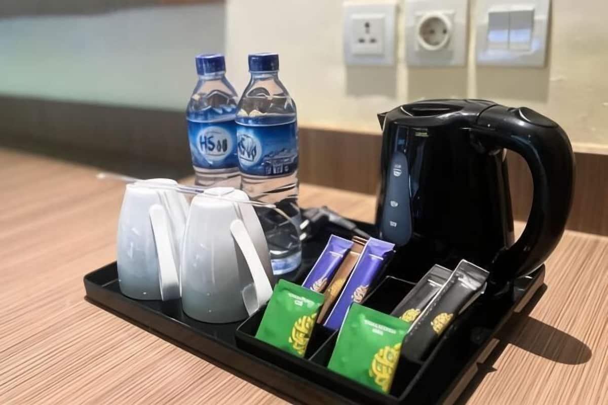 A hotel room's breakfast tray with two water bottles, two white mugs, a black coffee maker, and a few packets of snacks.