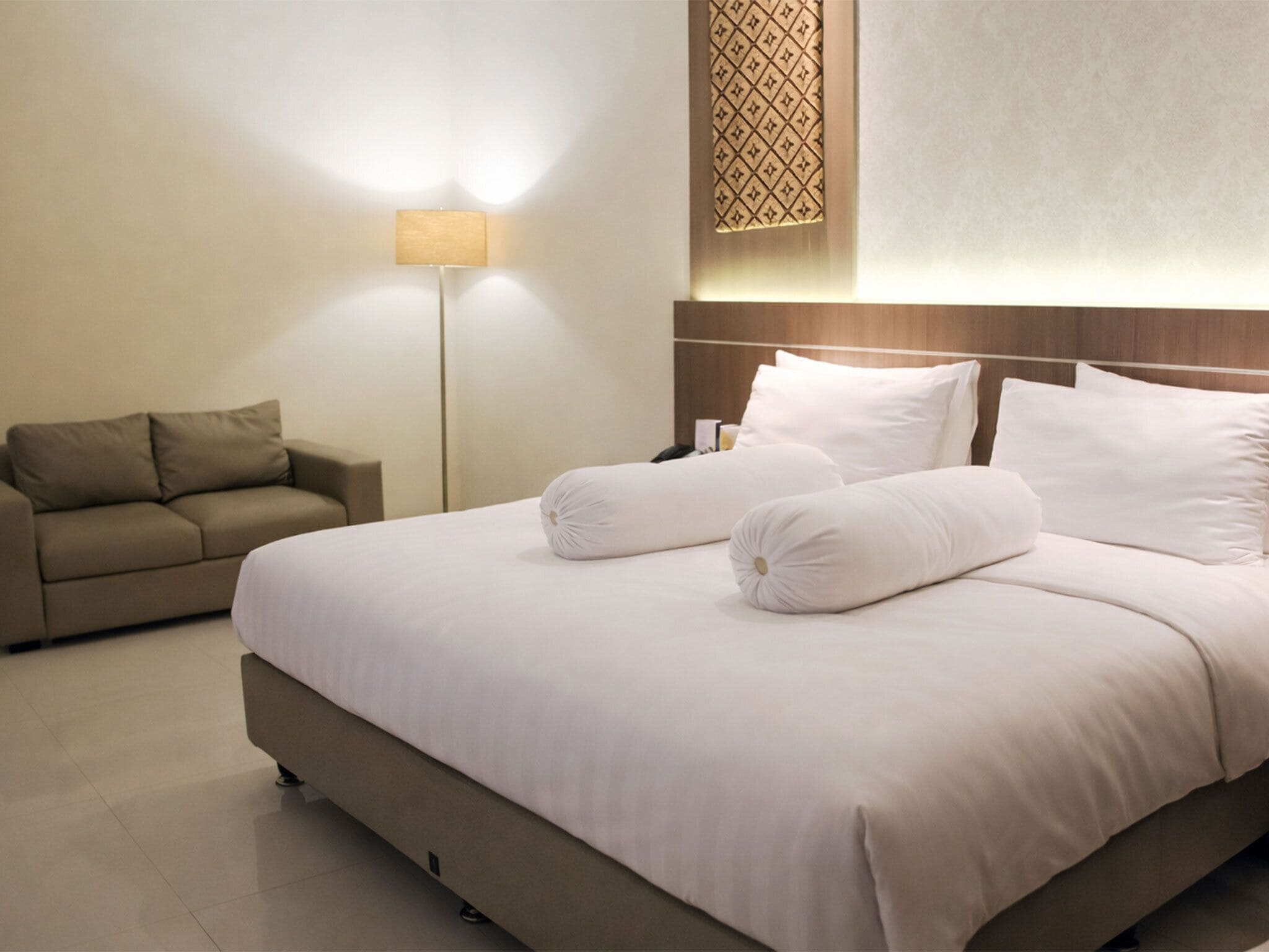 A hotel room with a large bed, a sofa, a bedside table, and a floor lamp.