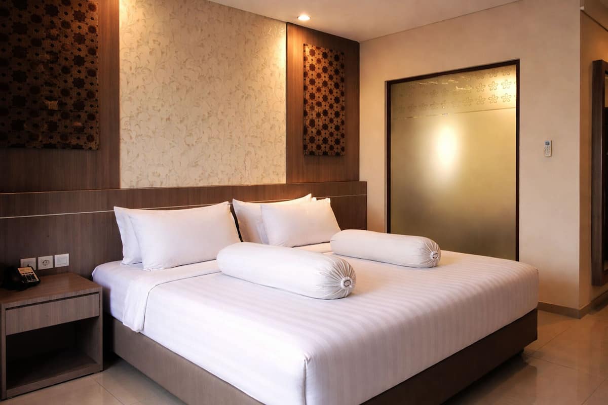 A modern hotel room with a large bed, a wooden headboard, a nightstand, and a wall-mounted phone.