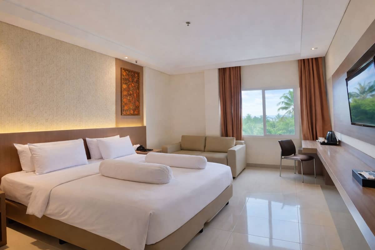 A modern hotel room with a large bed, a sofa, a desk, and a large window with a view of greenery.