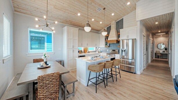 Una cocina moderna con armarios blancos, una isla central con taburetes y un comedor con sillas de mimbre.