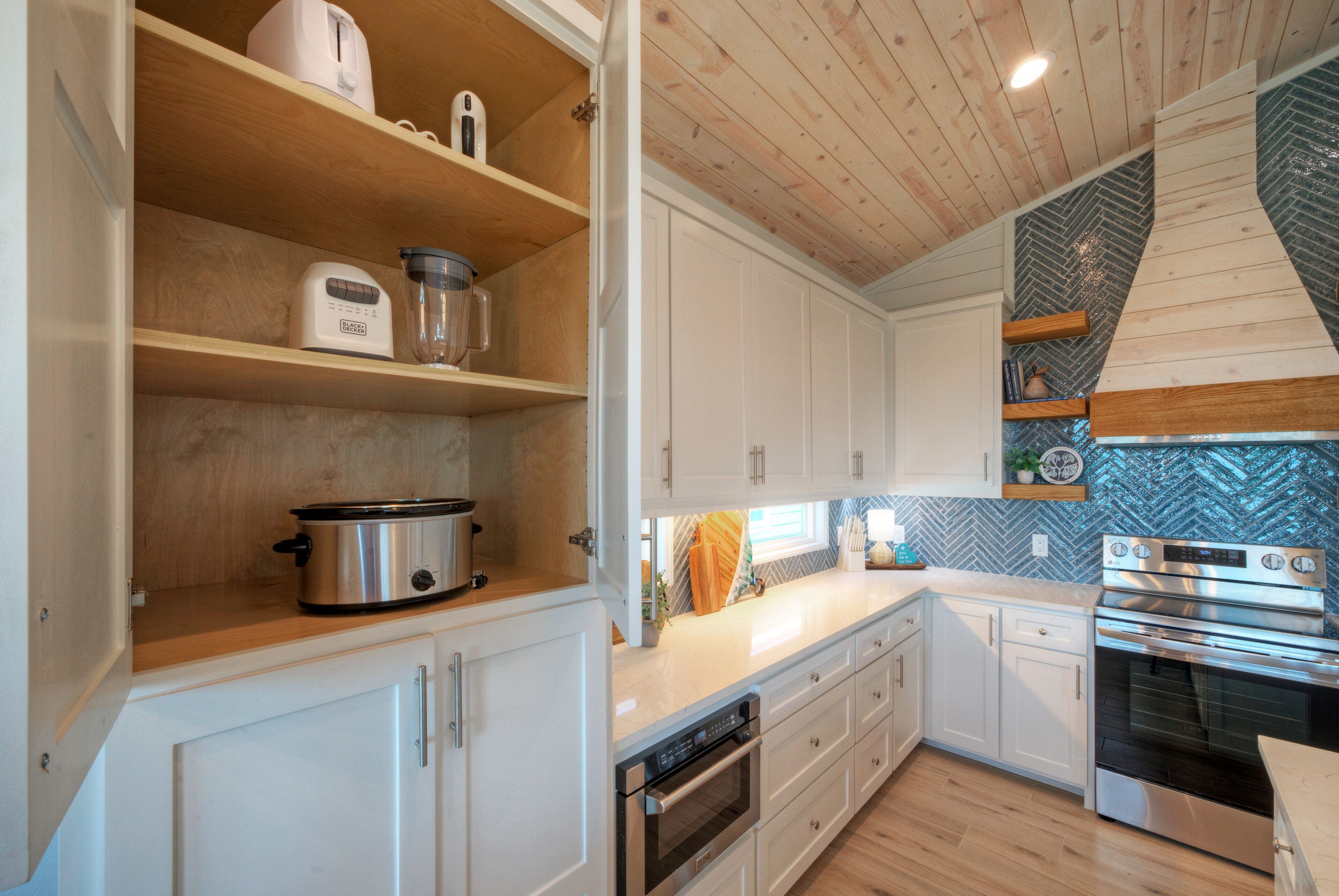 A modern kitchen with white cabinets, wooden shelves, and stainless steel appliances including a stove, oven, and dishwasher.
