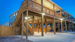 A two-story wooden house with a balcony and a staircase leading to the upper floor. - Pool, Firepit + Golf Cart Zone + Near Beach | Looney Dunes (Port Aransas)