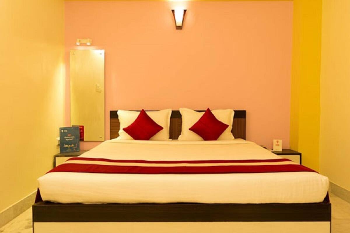 A hotel room with a bed, a nightstand, a mirror, and a wall-mounted light fixture.