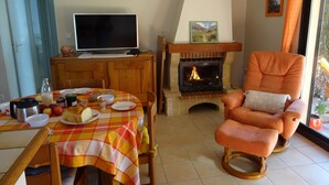 Un salon chaleureux avec une cheminée, un téléviseur et un coin repas avec une table mise pour deux personnes.