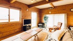 Una habitación acogedora estilo cabaña, con paredes de madera, un ventanal grande, televisor, una mesa de comedor y un rincón de estar cómodo.