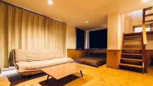 Una habitación acogedora con un sofá, una mesita, una ventana con cortinas y una escalera de madera.