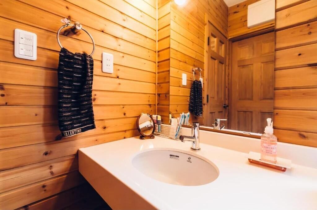 Un bagno in stile baita con legno a vista, dotato di lavabo, specchio, porta asciugamani e articoli da toilette.
