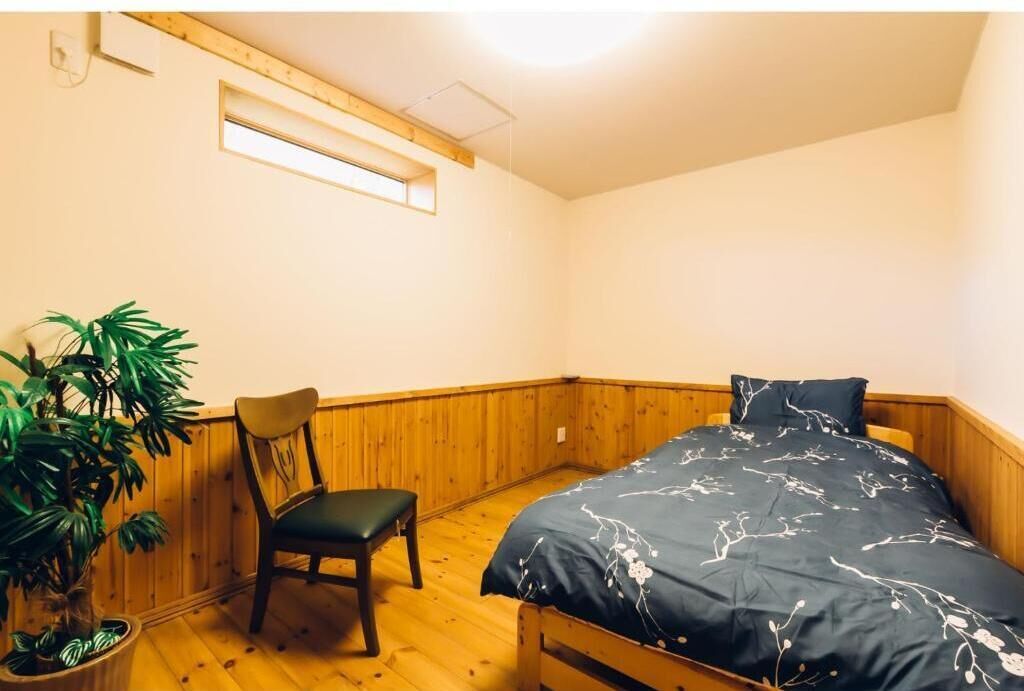 A small, cozy room with a bed, a chair, and a potted plant.