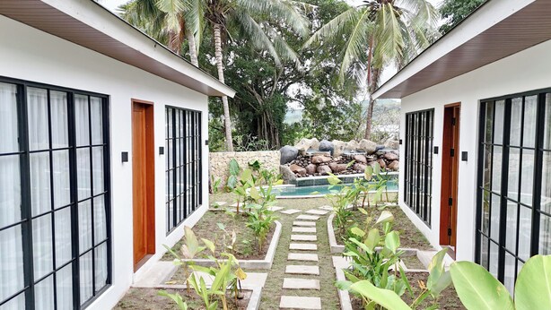 A pathway leading to a pool with a stone wall and palm trees in the background. - Malasama suites hotel (Kuta)