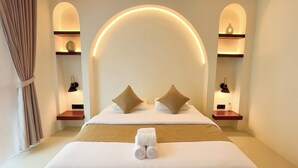 A hotel room with a large bed, two bedside tables, a wall arch, and built-in shelves with decorative items. - Malasama suites hotel (Kuta)