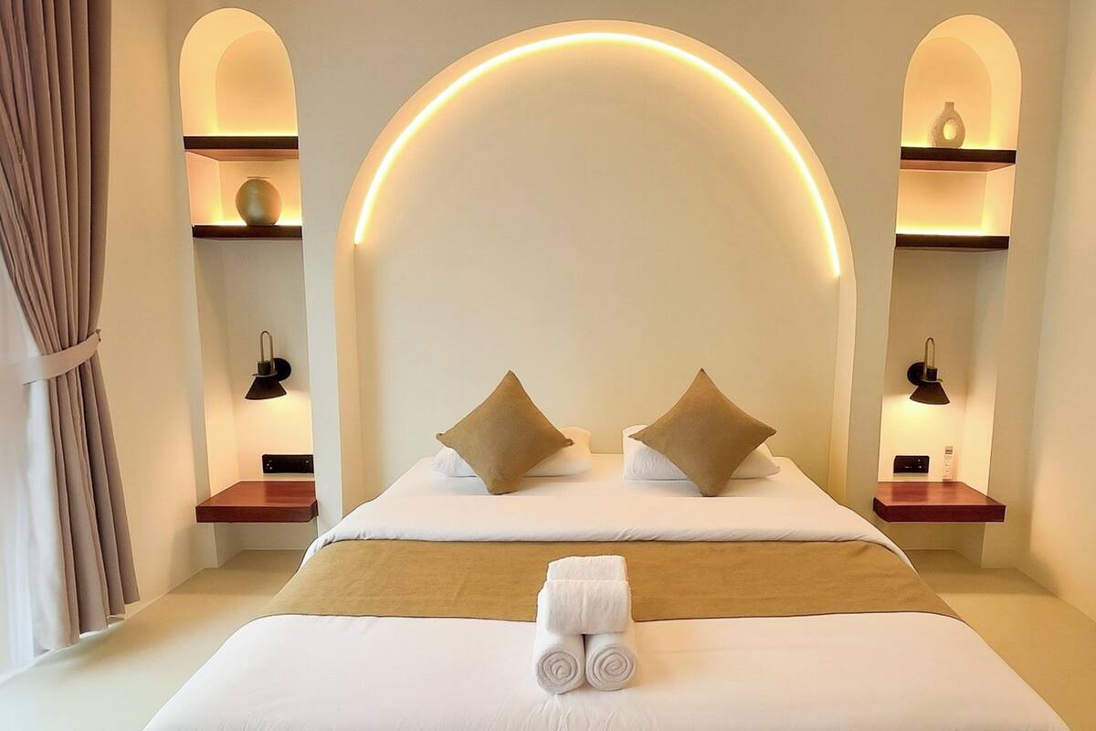 A hotel room with a large bed, two bedside tables, a wall arch, and built-in shelves with decorative items.