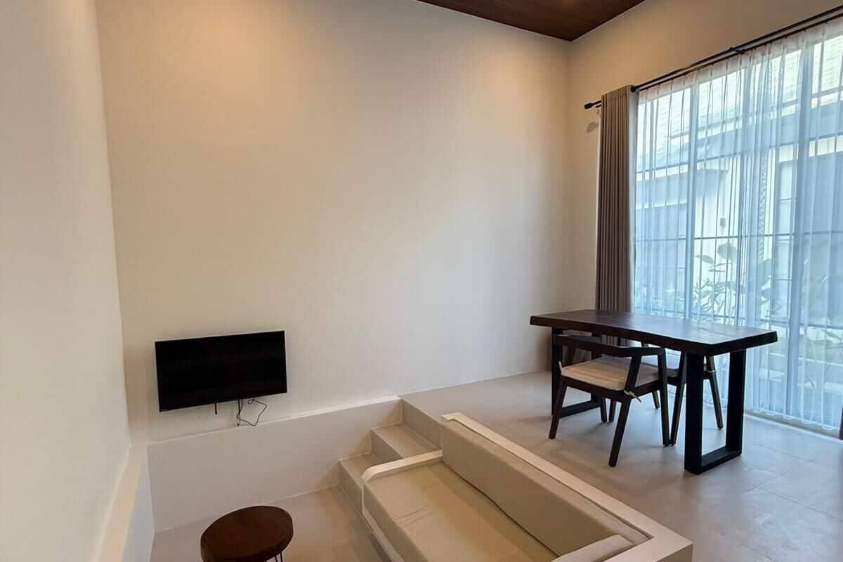 A modern living room with a built-in seating area, a flat-screen TV mounted on the wall, and a dining table with chairs.