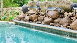 A pool with a waterfall feature, surrounded by large rocks and a stone wall. - Malasama suites hotel (Kuta)