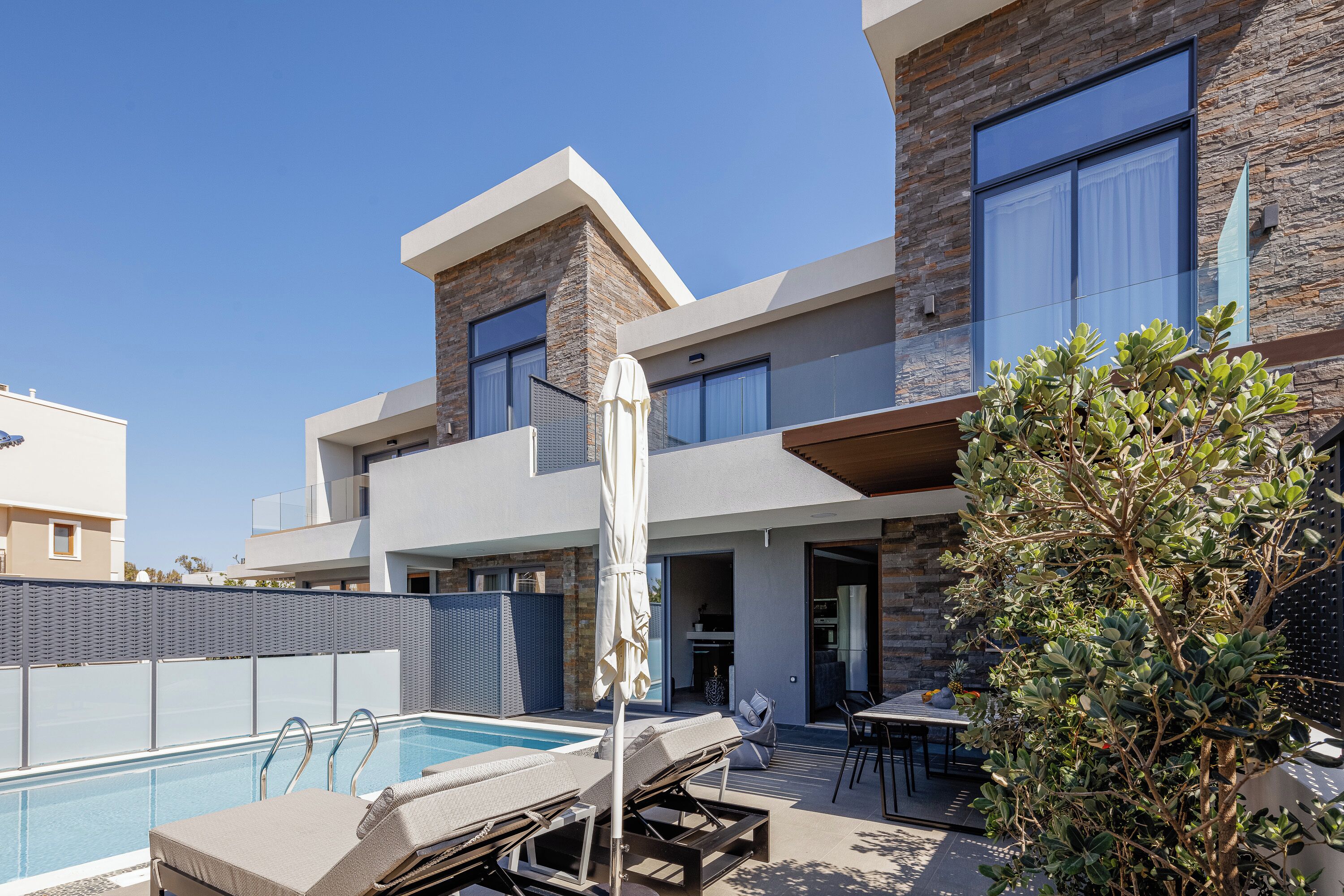 A modern two-story building with a swimming pool, outdoor seating, and a stone facade.