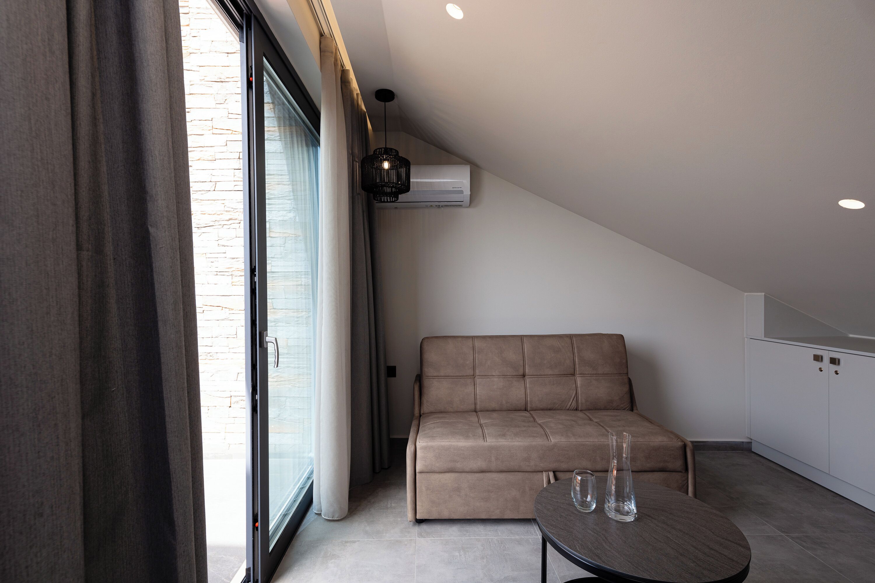 A modern living room with a sofa, a glass table, and an air conditioning unit mounted on the wall.