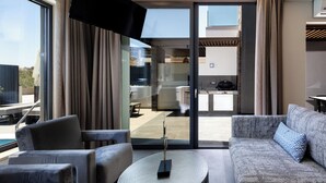 A modern living room with a sofa, armchairs, and a coffee table. There is a large window with curtains, a flat-screen TV mounted above the sofa, and a view of the outdoor patio area. - VillAgioi IIΙ - Stylish Pool Villa, 450m to Sandy Beach (Chania)