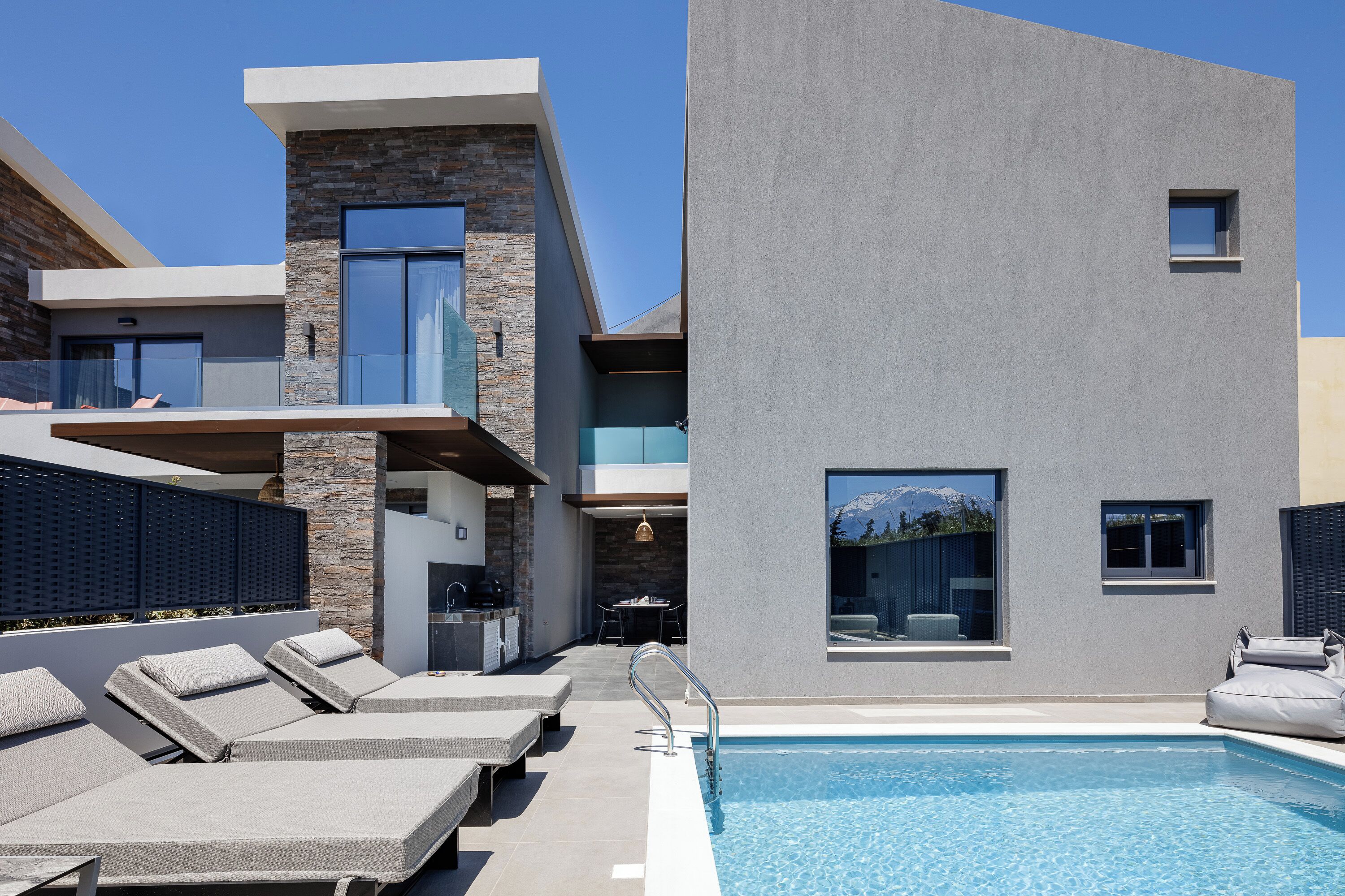 A modern poolside area with lounge chairs, a pool, and a contemporary building with stone and concrete elements.